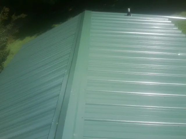 New green metal panels meeting at the ridge of a roof — Flat Roof Repair work by our crew in Ocala