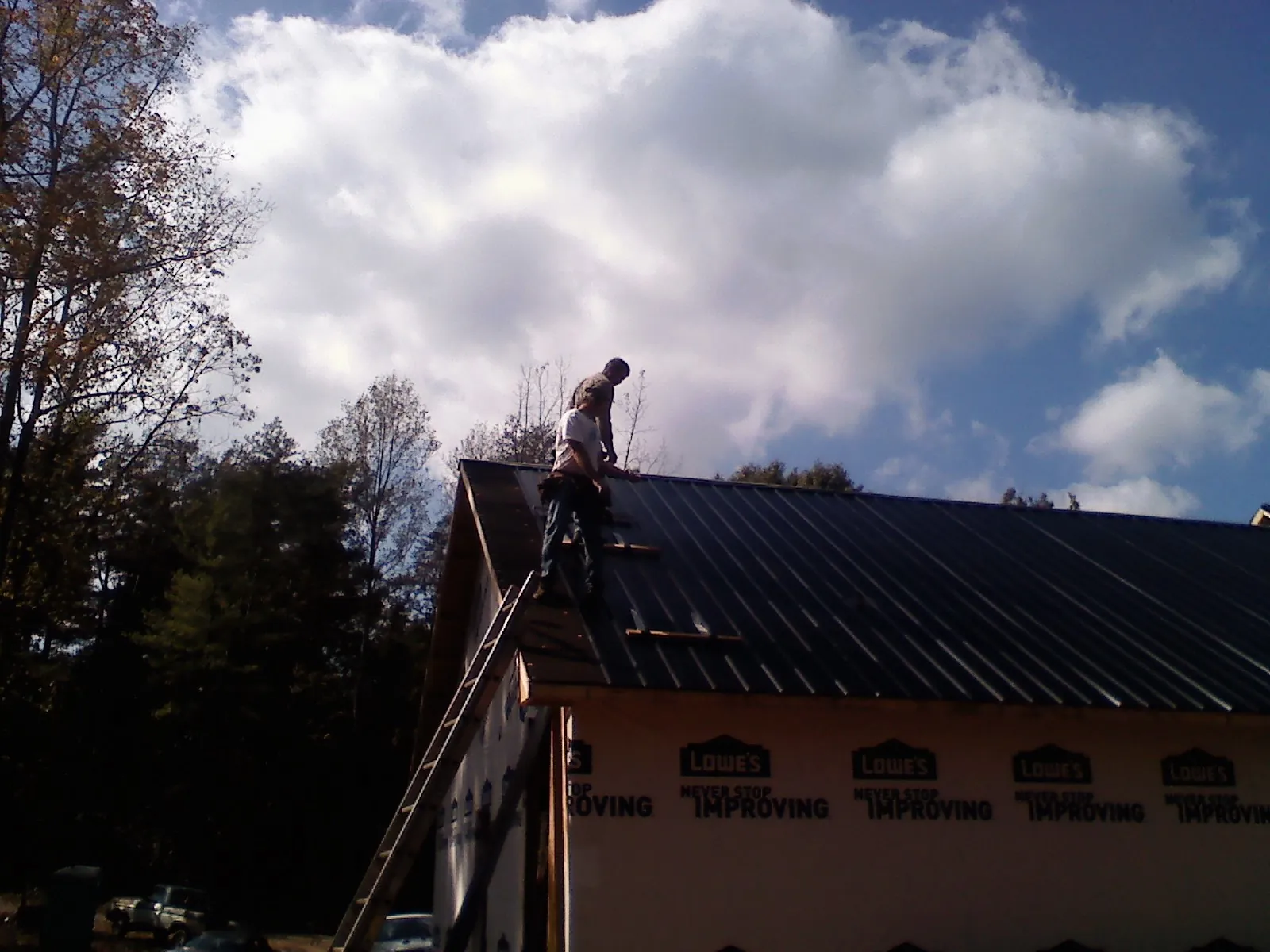 Roofer fastening dark metal panels high against a cloudy sky, from a Roof Inspection job in Ocala